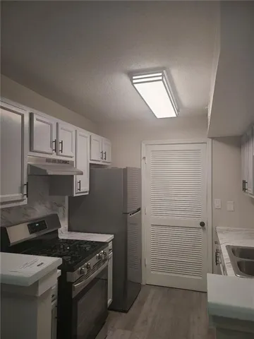 Kitchen featuring stainless steel appliances, light countertops, a textured ceiling, white cabinetry, and dark wood-style floors