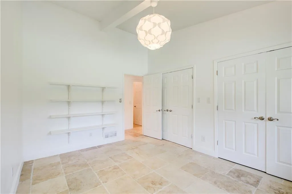 Unfurnished bedroom with stone finish flooring, beamed ceiling, multiple closets, baseboards, and a chandelier