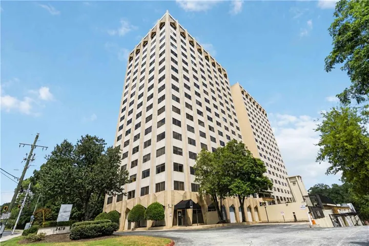 Multi-story building featuring numerous windows, a prominent entrance canopy, and established exterior landscaping