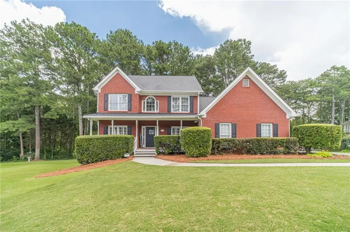 Two-story brick exterior with a covered front porch, arched window, and mature landscaping