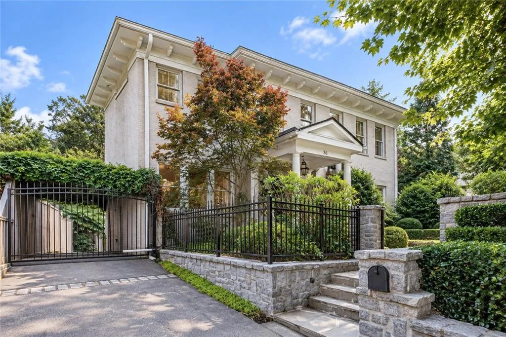 Stately brick exterior, portico entry, stone retaining walls, mature landscaping, and an automatic gate entrance