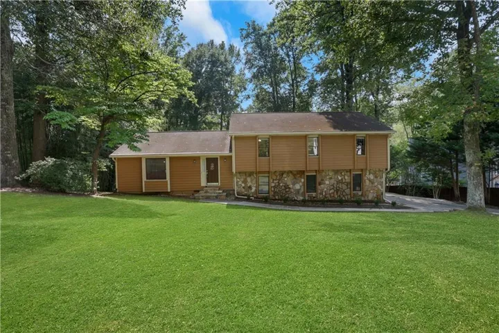 Split-level exterior with siding and stone facade, featuring a front lawn, mature trees, and a paved driveway