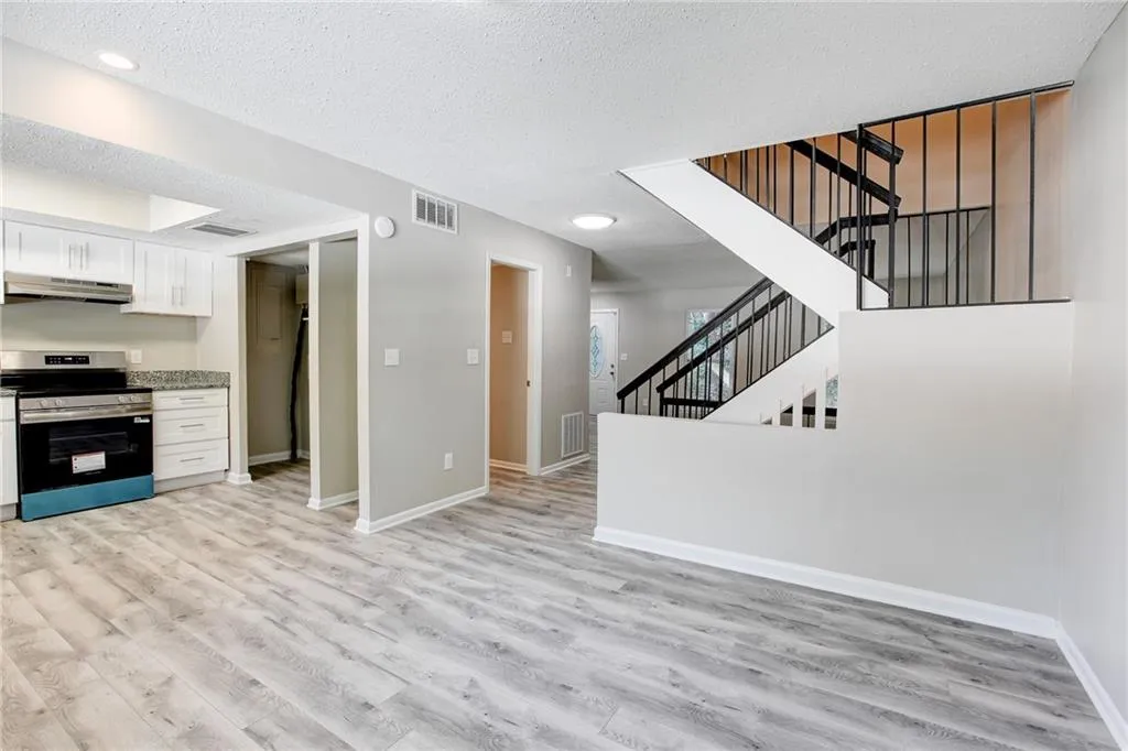 Kitchen with stainless steel electric range oven, a textured ceiling, white cabinets, light wood-style floors, and under cabinet range hood