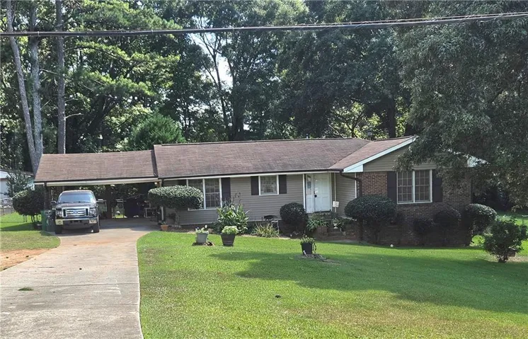 Single-story residence featuring a carport, a concrete driveway, and a front lawn with established landscaping