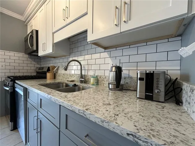 Updated kitchen featuring two-tone cabinetry, a dual-basin stainless steel sink with a gooseneck faucet, a subway tile backsplash, and speckled countertops