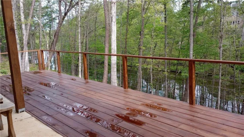 Expansive wood-plank deck with cable railing overlooking a wooded landscape and body of water