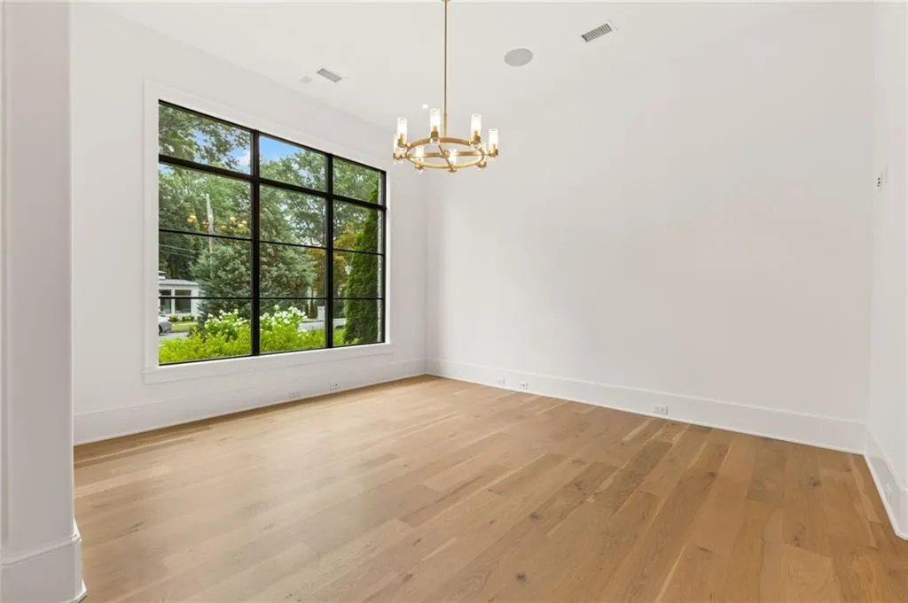 Expansive window with black grid panes, light wood-finish flooring, white walls, and a contemporary brass chandelier