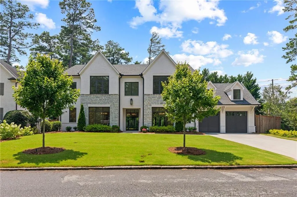 Contemporary two-story residence featuring a white brick and stone facade, a two-car garage with dormer, black frame windows, and a landscaped front lawn
