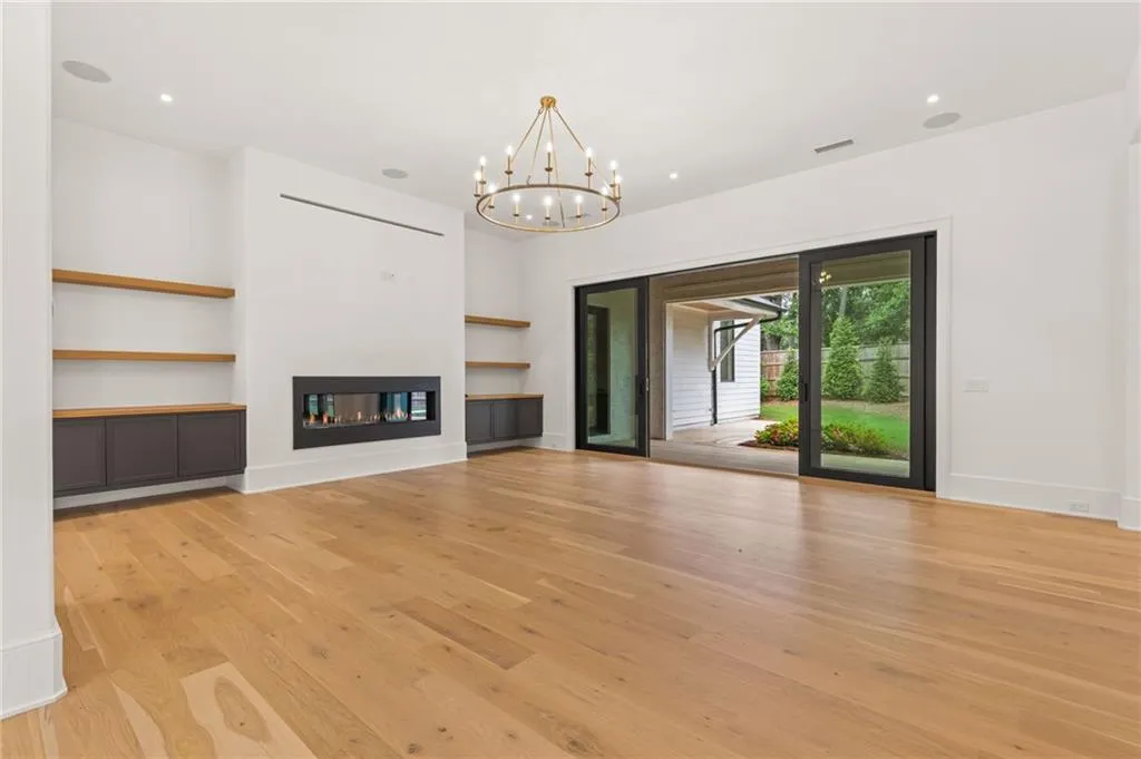 Spacious interior featuring wide-plank wood-finish flooring, a linear fireplace, custom built-in cabinetry with wood shelving, and large sliding glass doors leading to the outdoor area