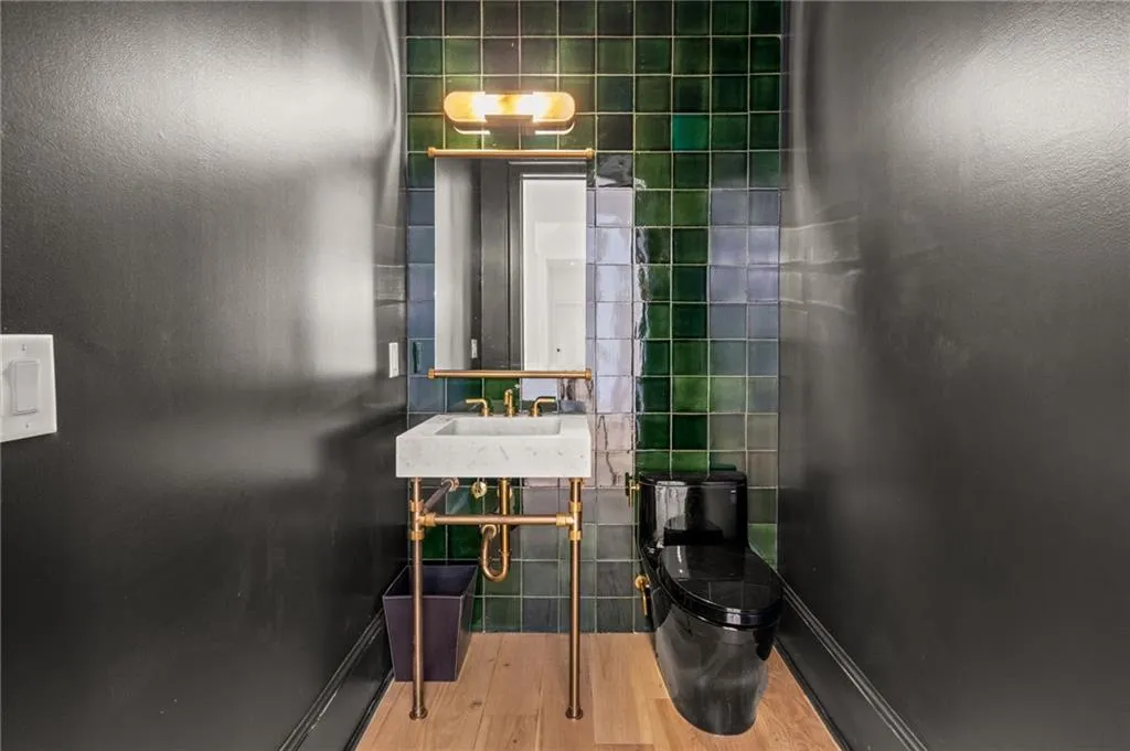 Powder room featuring a square vessel sink on a brass-finish console, a black toilet, and green and blue wall tiles