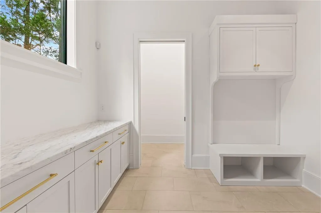 White built-in cabinetry with gold-tone hardware, a light-toned countertop, and light-colored tiled flooring