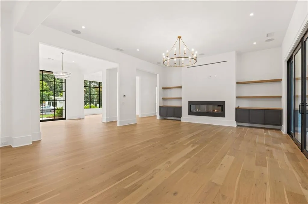 Spacious room featuring wood-finish flooring, a linear fireplace with a white surround, built-in shelving with lower cabinetry, and a prominent chandelier