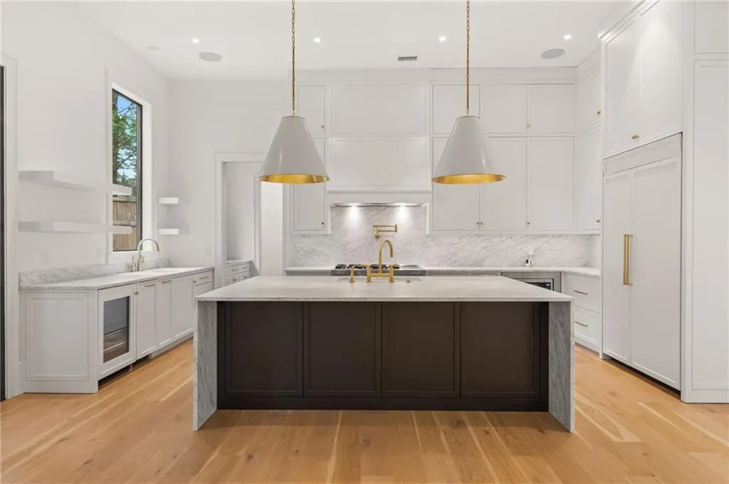 Expansive chef's kitchen featuring a large central island with a waterfall countertop, integrated paneled refrigerator, built-in wine cooler, hardwood flooring, and elegant pendant lighting