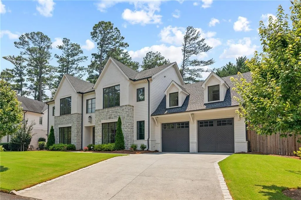 Contemporary residence featuring a light-colored brick and stone facade, expansive black-framed windows, a two-car garage with dormer accents, a concrete driveway with paver edging, and a manicured lawn