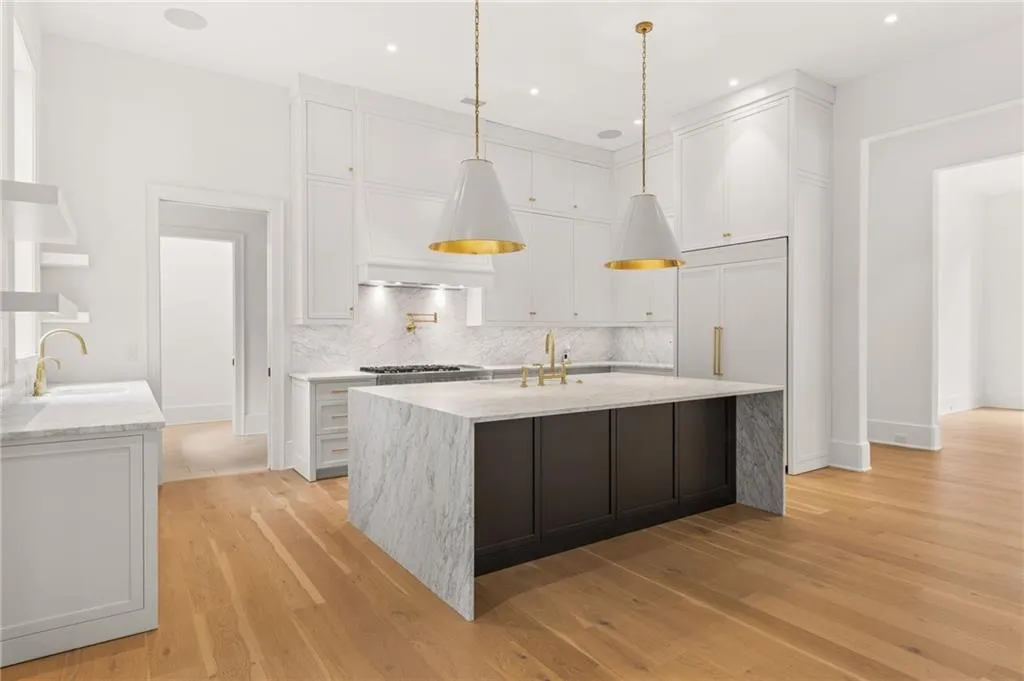 Contemporary kitchen featuring a waterfall island with stone countertop, brass fixtures, integrated refrigerator, white cabinetry, and wood-finish flooring