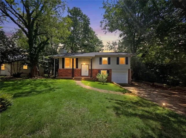 Split-level residence featuring a brick and siding exterior, an attached garage, a paved driveway, and mature landscaping