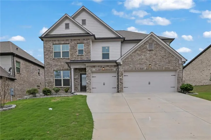 Two-story residence featuring a brick and siding exterior, a two-car garage with carriage-style doors, a concrete driveway, and a manicured front lawn