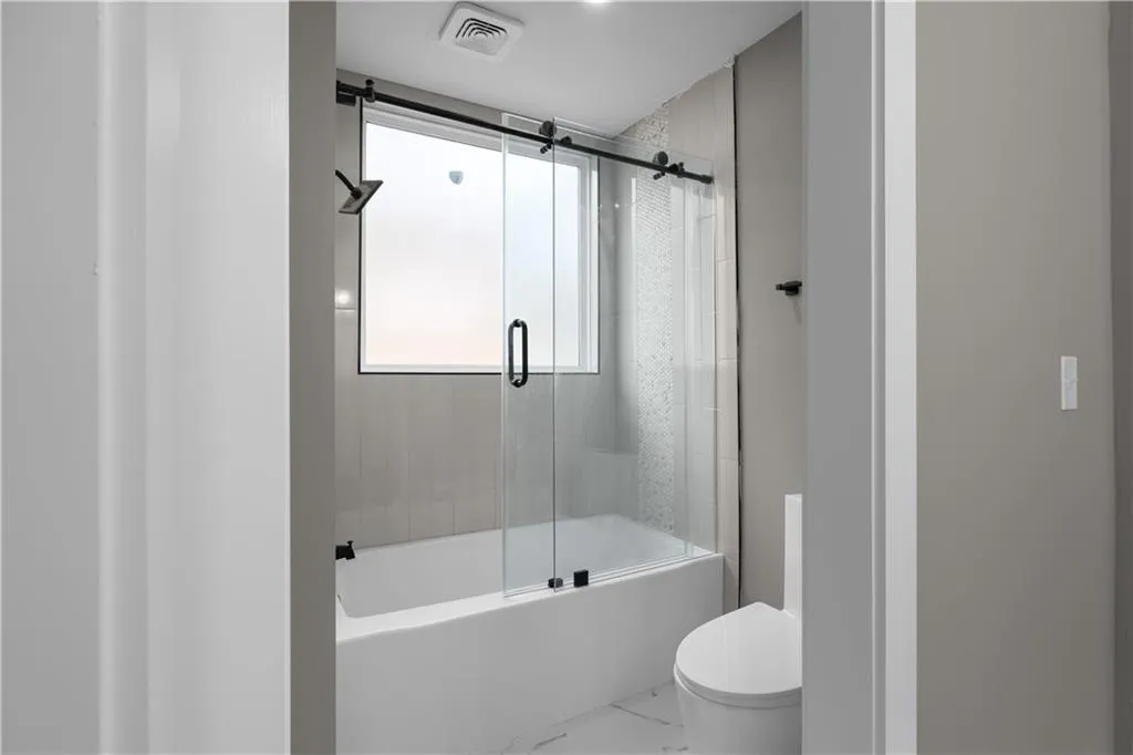 Bathroom with combined bath / shower with glass door and marble finish flooring