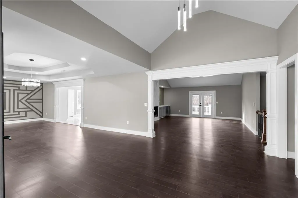 Unfurnished living room with french doors, lofted ceiling, dark wood-style flooring, a chandelier, and ornate columns