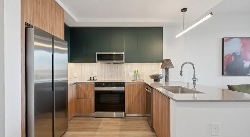 Kitchen featuring stainless steel appliances, a peninsula, modern cabinets, light stone counters, and hanging light fixtures