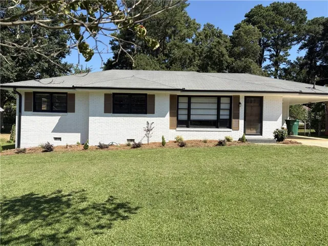 White brick exterior with a gray shingle roof, dark-framed windows, and brown decorative shutters