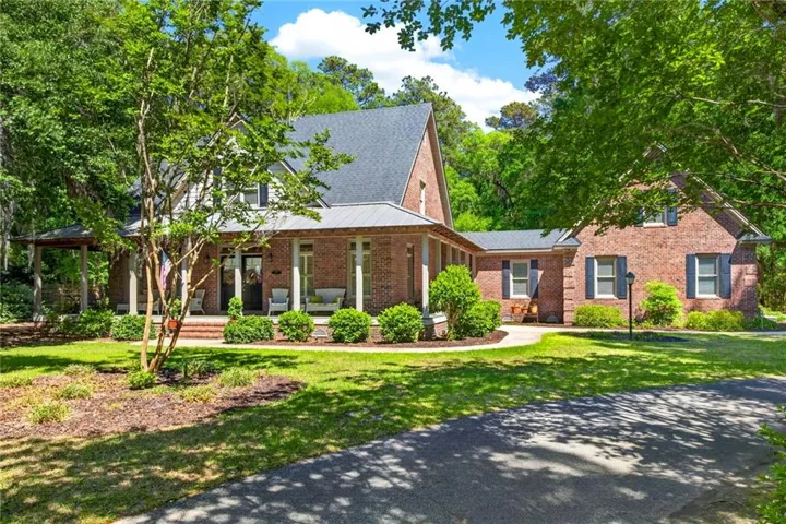 Brick exterior with a covered front porch featuring columns, a dark shingle roof, and established landscaping