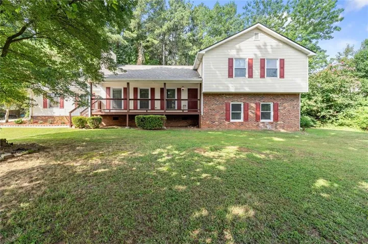 Two-story brick and siding residence with a covered front porch, red shutters, and a manicured lawn anchored by mature shade trees