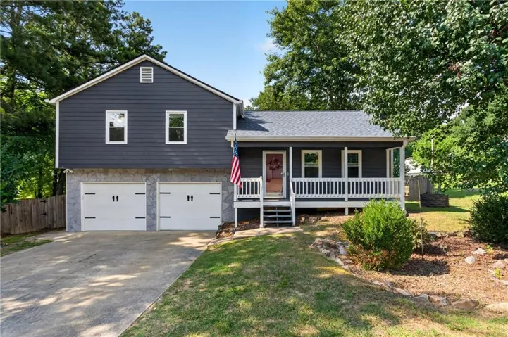 Split-level residence featuring dark siding, a white-railed porch, stone-accented foundation, and a two-car garage with carriage-style doors