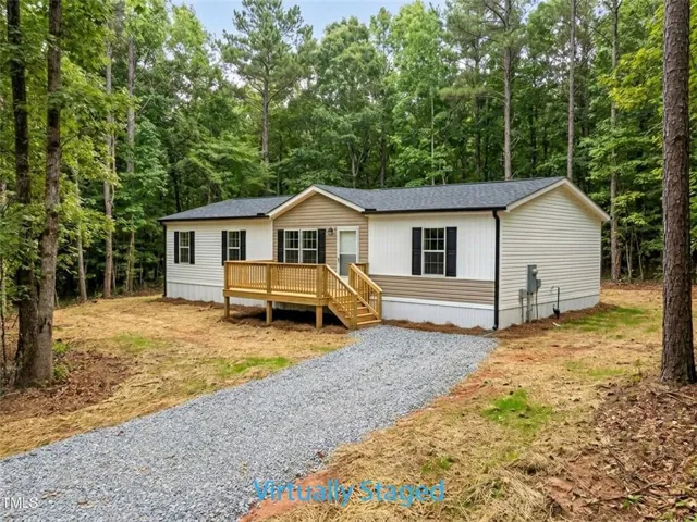 Gravel driveway leading to a home with a wooden deck, dark shingle roof, and exterior siding