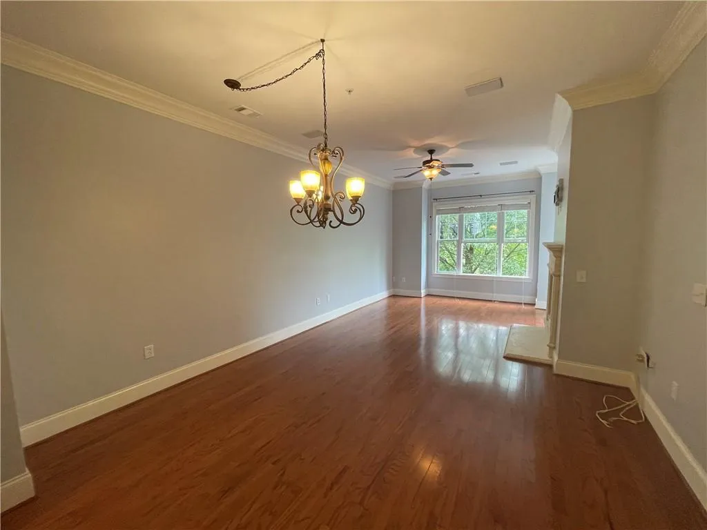 Empty room with crown molding, dark wood-style floors, a chandelier, and a ceiling fan