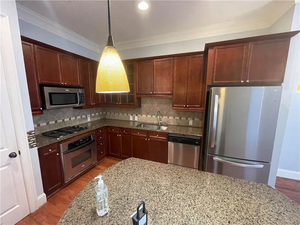 Kitchen with appliances with stainless steel finishes, crown molding, dark stone countertops, decorative backsplash, and decorative light fixtures