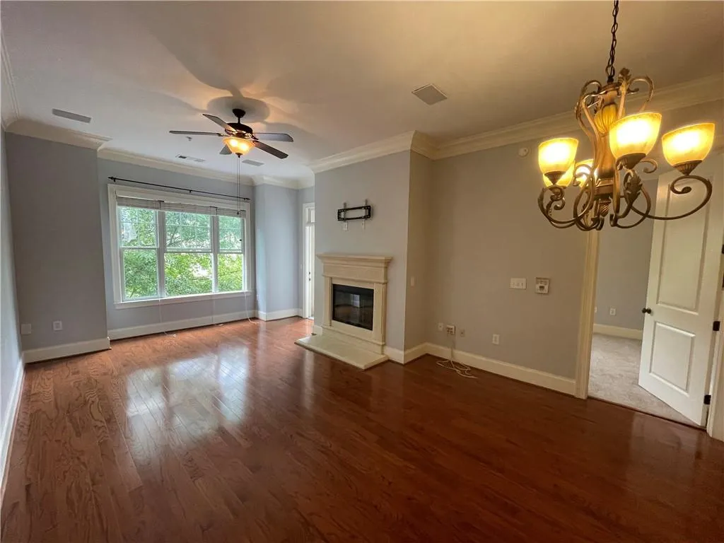 Unfurnished living room with crown molding, a glass covered fireplace, dark wood-style floors, a chandelier, and ceiling fan
