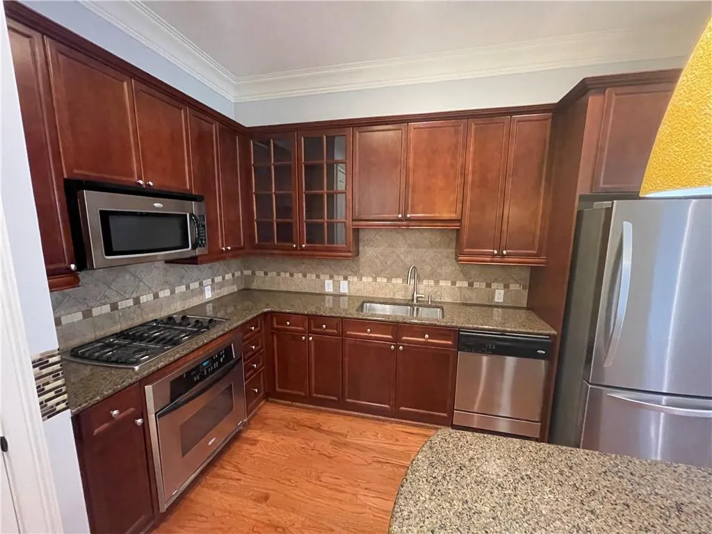 Kitchen with appliances with stainless steel finishes, dark stone countertops, crown molding, glass insert cabinets, and light wood-type flooring