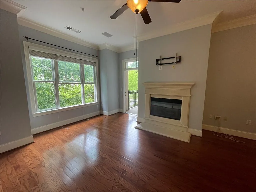 Unfurnished living room featuring ornamental molding, a glass covered fireplace, wood finished floors, and ceiling fan