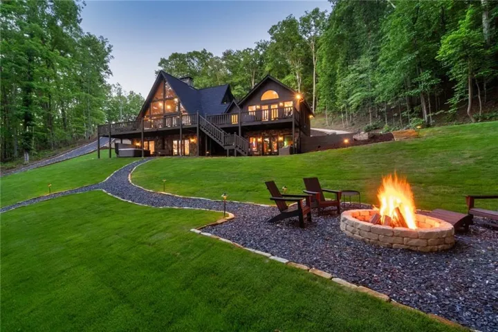 Back house at dusk featuring a wooden deck, lush lawn, and an outdoor fire pit