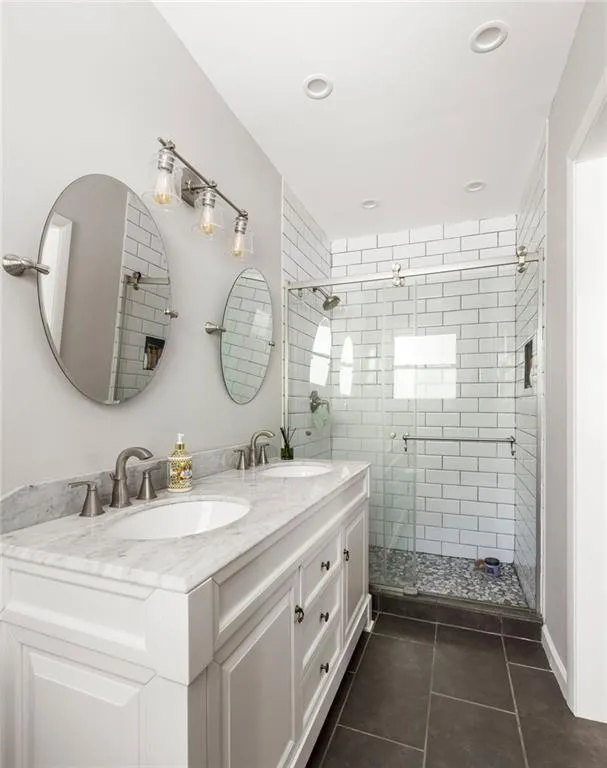 Bathroom with dual vanity, tile patterned floors, and an enclosed shower
