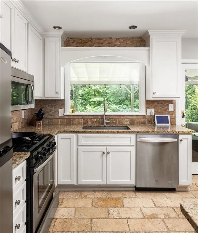 Kitchen featuring dark stone counters, white cabinetry, tasteful backsplash, stainless steel appliances, and sink
