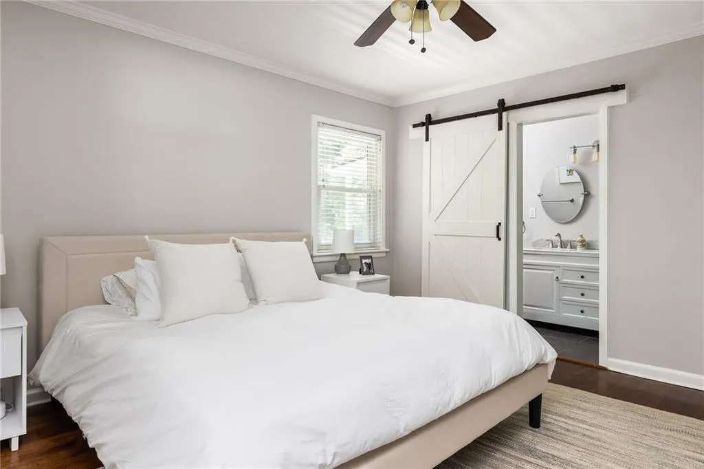 Bedroom featuring dark hardwood / wood-style flooring, ensuite bathroom, a barn door, and ceiling fan