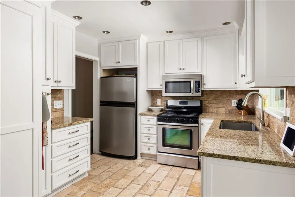 Kitchen featuring tasteful backsplash, white cabinets, light stone countertops, appliances with stainless steel finishes, and sink