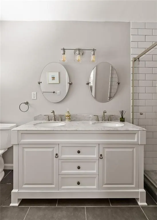 Bathroom featuring a shower with shower door, toilet, tile patterned flooring, and double vanity