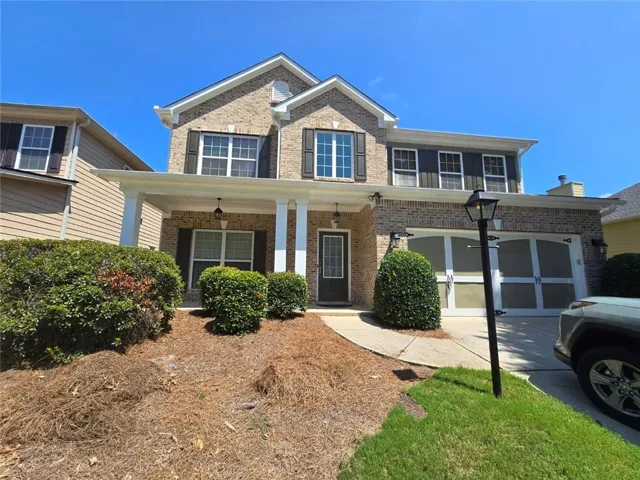 Brick facade with white trim, covered front porch, attached two-car garage, and mature shrubbery
