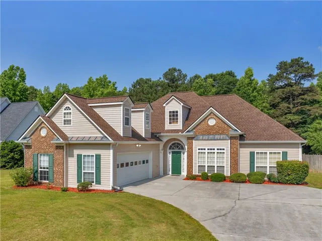 Traditional-style home featuring driveway, brick siding, an attached garage, and roof with shingles