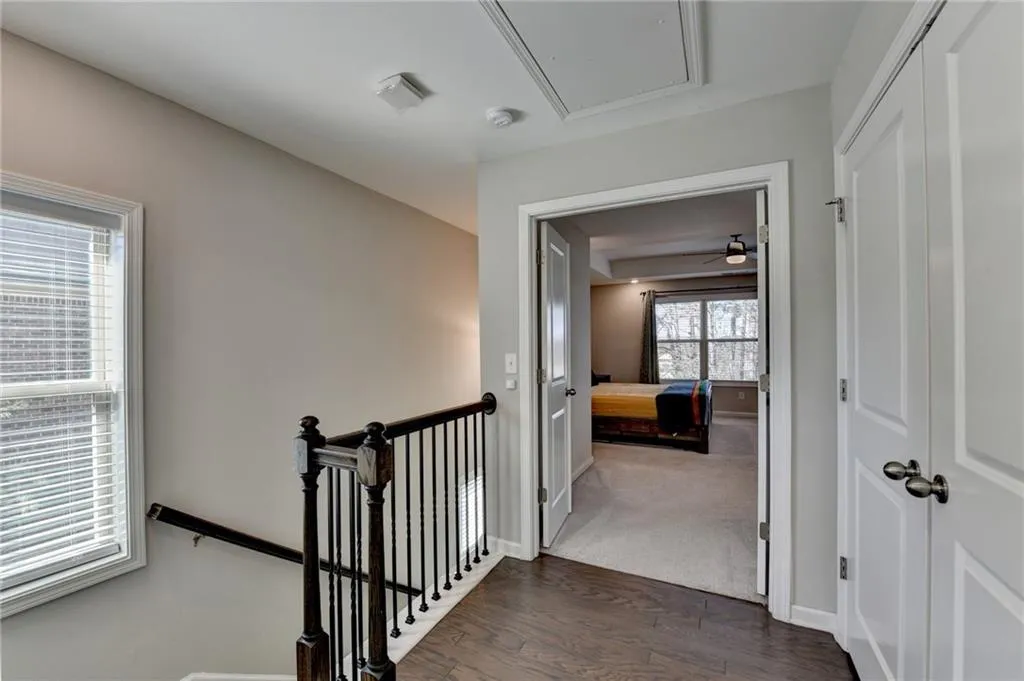 Hallway with dark wood-type flooring, an upstairs landing, baseboards, dark colored carpet, and attic access