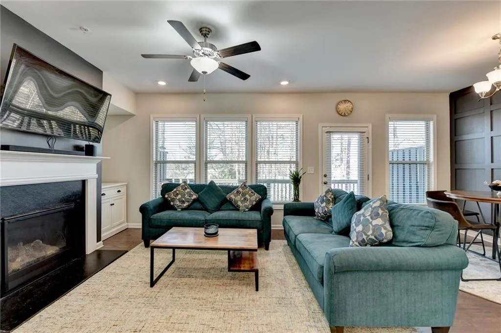 Living room with dark wood-style flooring, a glass covered fireplace, a ceiling fan, and recessed lighting