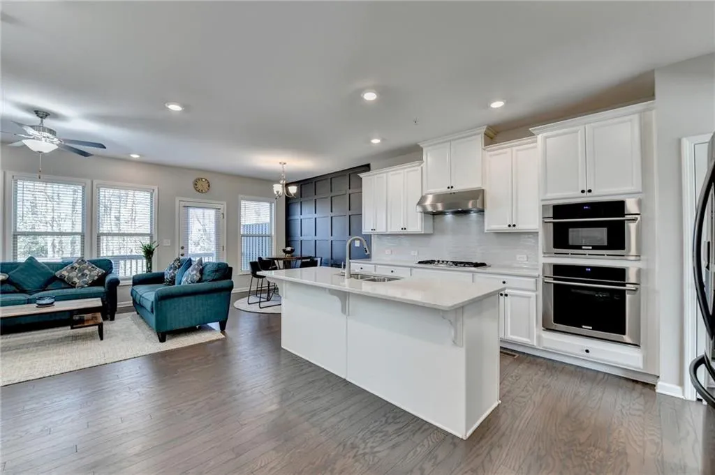 Kitchen featuring under cabinet range hood, decorative backsplash, open floor plan, and a sink