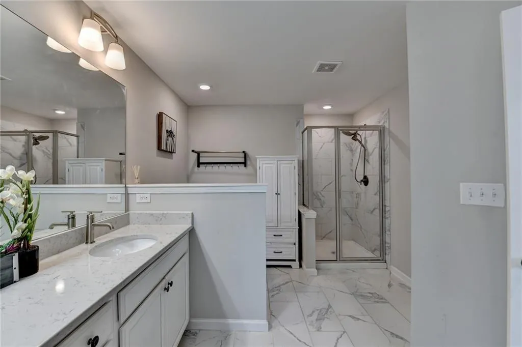 Full bath featuring marble finish floor, visible vents, a stall shower, and vanity