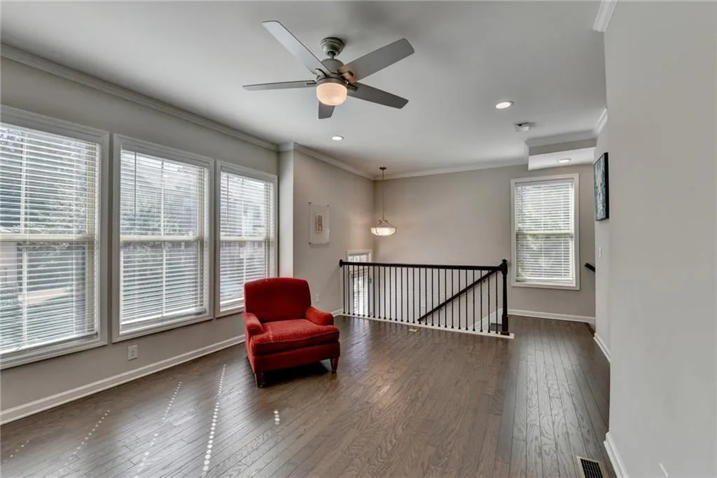 Living area with dark wood-style flooring, crown molding, visible vents, an upstairs landing, and baseboards