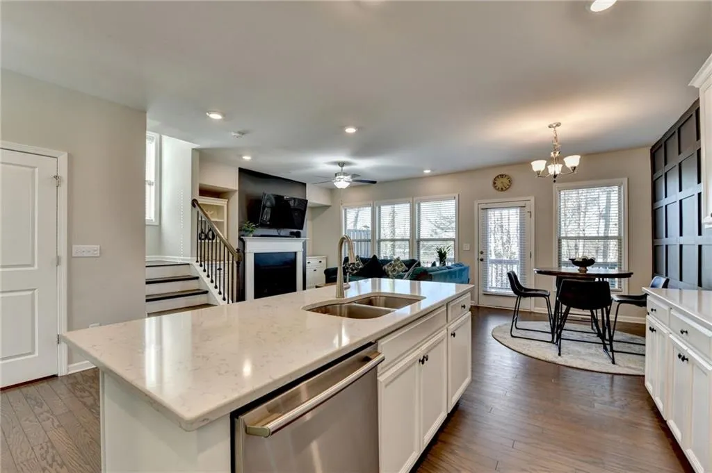 Kitchen featuring dark wood-type flooring, a fireplace, a sink, white cabinetry, and stainless steel dishwasher