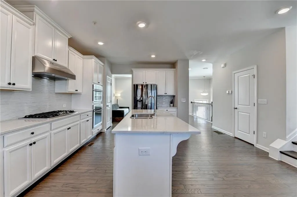 Kitchen with appliances with stainless steel finishes, white cabinetry, a sink, and under cabinet range hood
