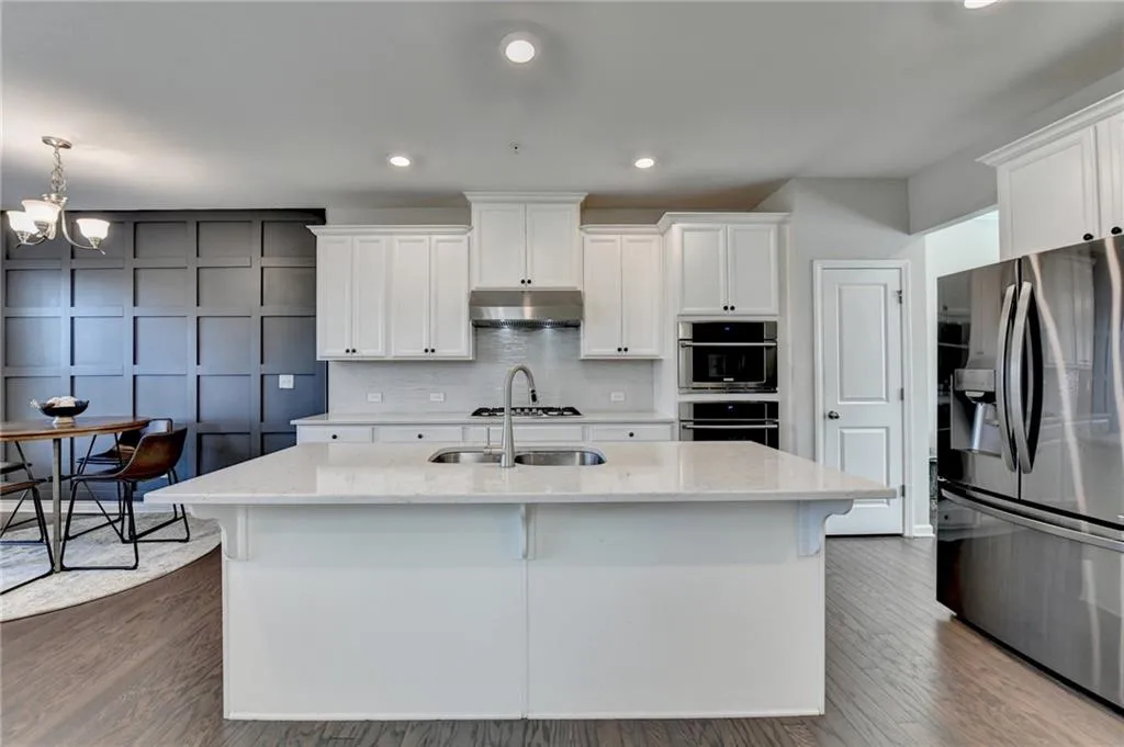 Kitchen featuring a decorative wall, under cabinet range hood, stainless steel appliances, white cabinets, and decorative backsplash